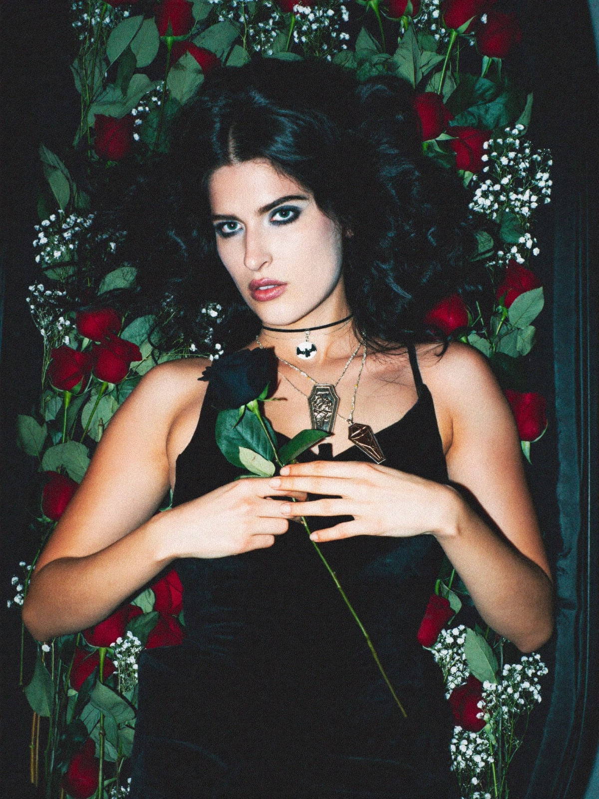 Model lying in a bed of dead roses, open-casket style, staring at camera